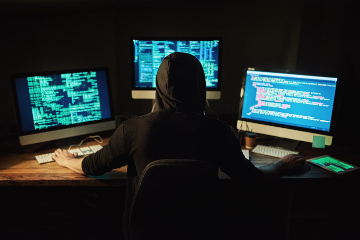 Rearview shot of a young hacker cracking a computer code in the dark.